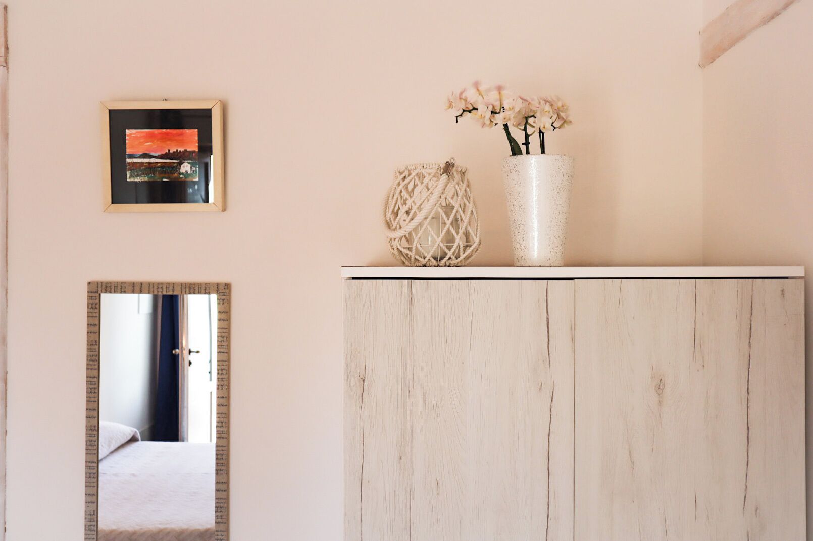 Ein Zimmer mit einem Holzkasten, einem Spiegel, einem gerahmten Gemälde und einer Vase mit Blumen.