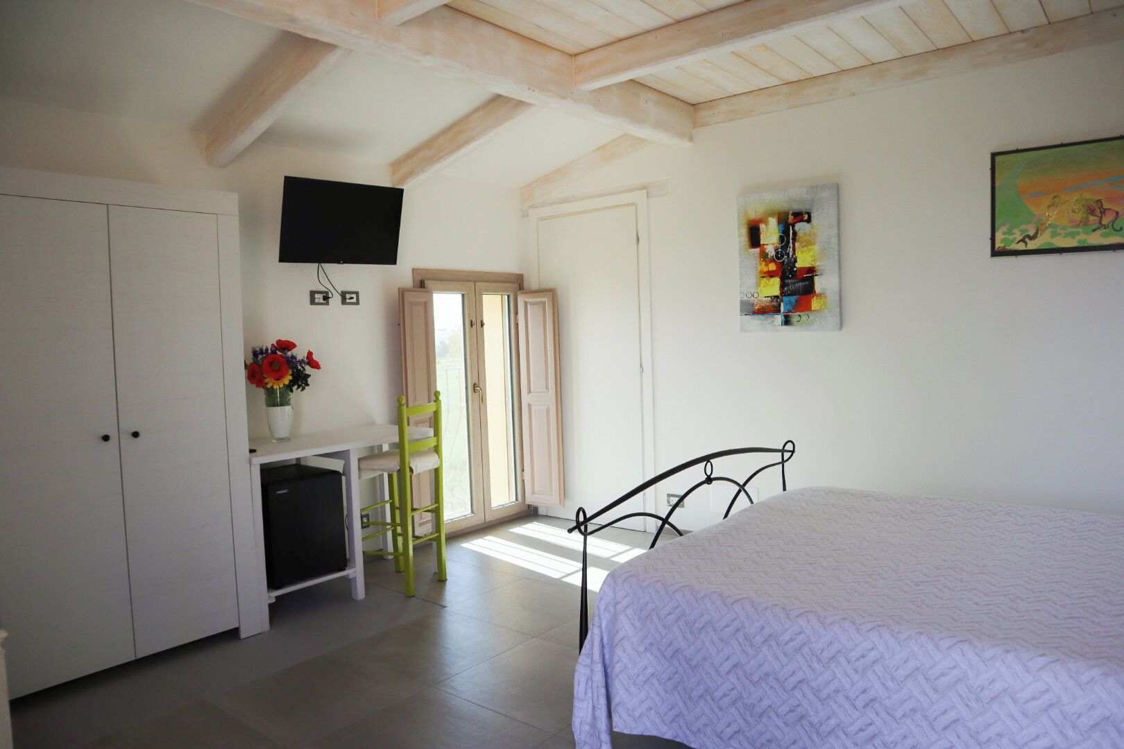 Ein Schlafzimmer mit einem Bett, einem Schreibtisch mit Stuhl, einem Fernseher und einer Tür, die auf einen Balkon führt.