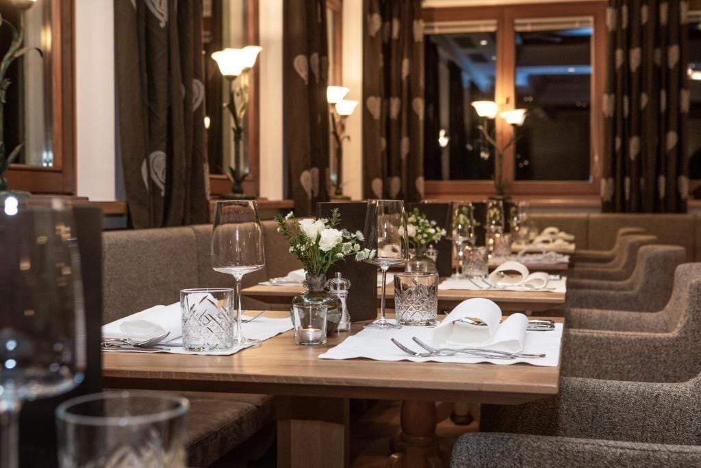 Un restaurante con mesas dispuestas para comer, con copas de vidrio transparente, servilletas blancas y centros de mesa con flores.