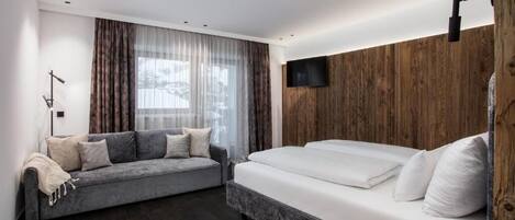 Un dormitorio moderno con sofá, cama, una mesita y televisor instalado en una pared de madera.