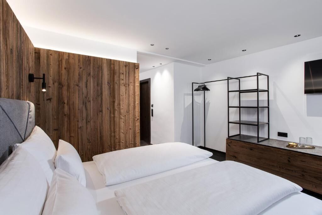 A modern hotel room with a wooden accent wall, a wardrobe, a bedside table, and a bed with white linens.