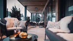 Un área de estar moderna al aire libre con sofás y sillones acolchados, una mesa redonda con una bandeja de comida y vistas del exterior a través de grandes ventanales.