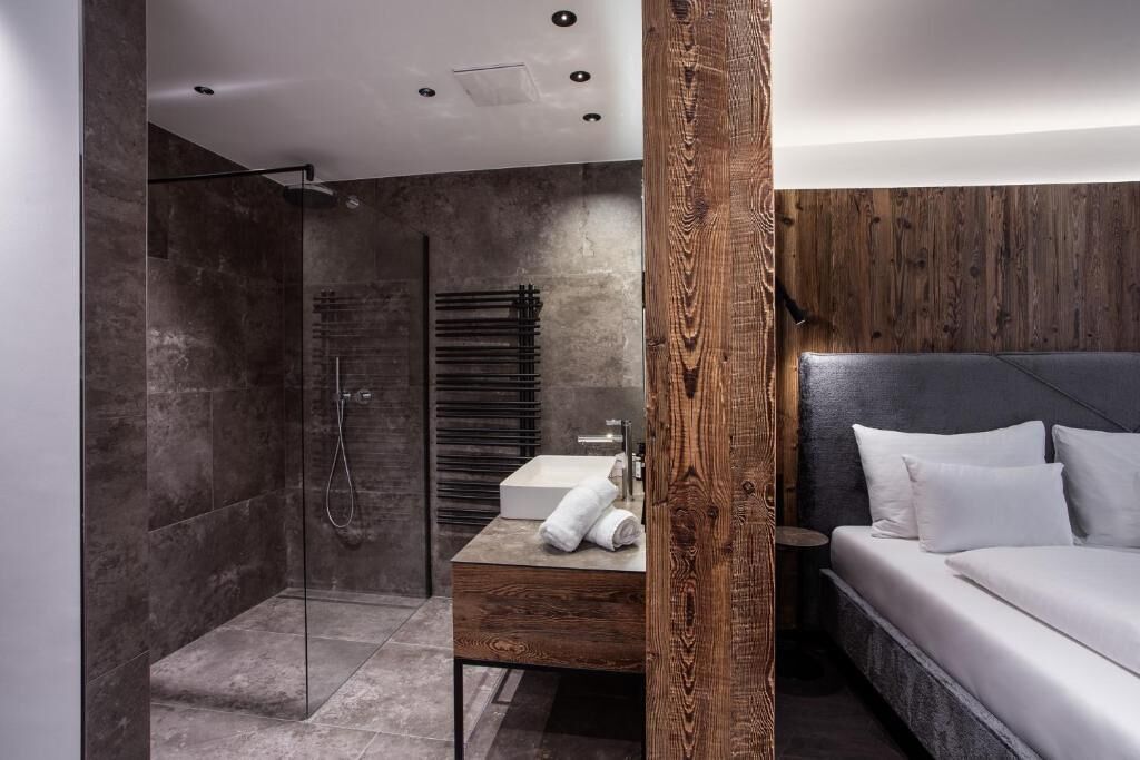 Een moderne badkamer met een glazen douche, een houten wastafelmeubel en een bed met wit beddengoed.