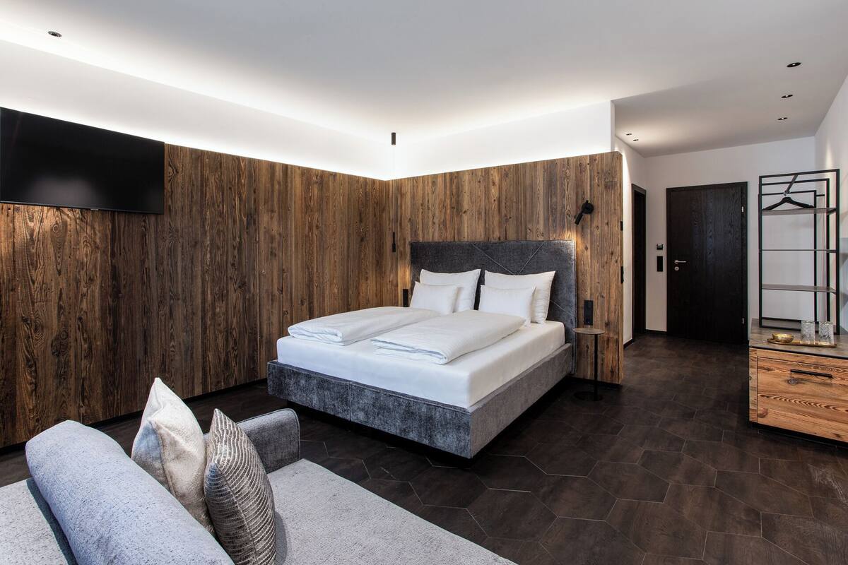 A modern bedroom with a large bed, wooden panel walls, a dark floor, and a minimalist design.