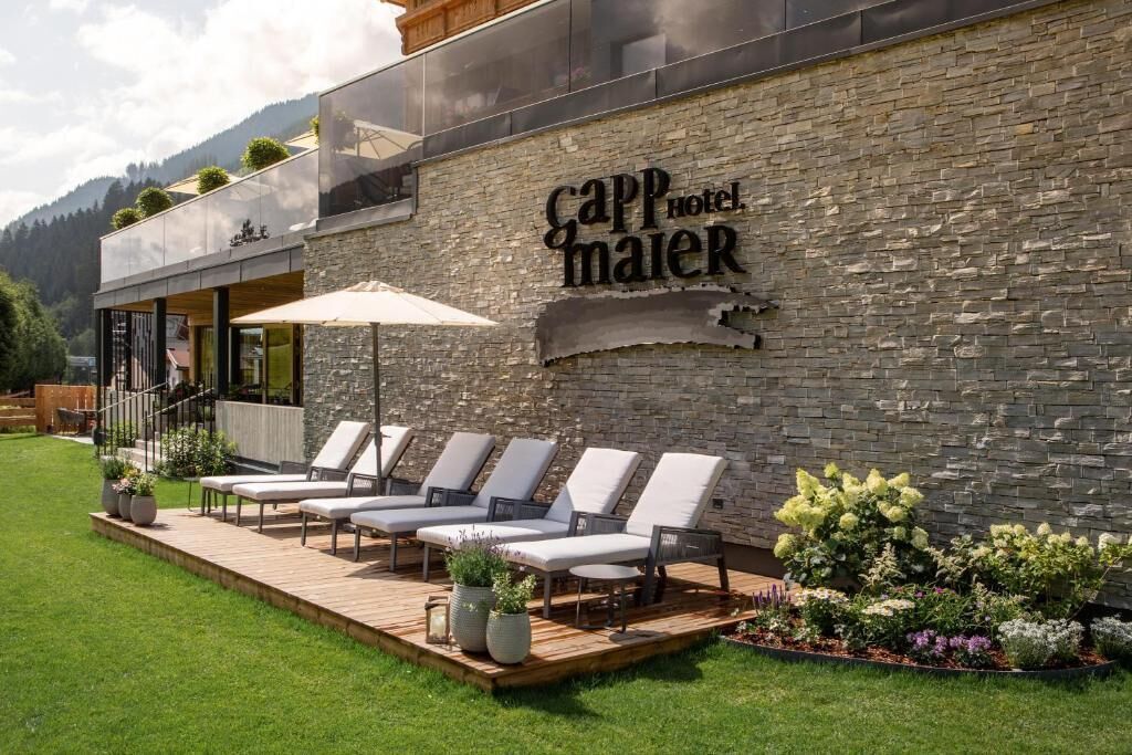 A hotel exterior with a stone wall, lounge chairs, and a wooden deck.