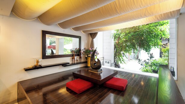 Um interior moderno com soalho de madeira escura, uma mesa central com um vaso de flores e um espelho grande na parede.