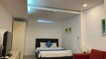 A hotel room with a bed, a TV, a desk, a red sofa, and a lamp.