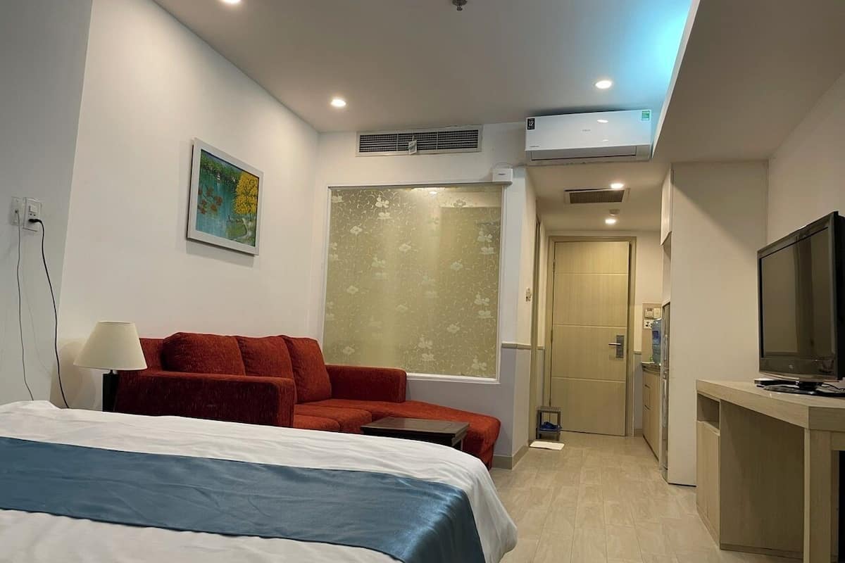 Una habitación de hotel con una cama, un sofá rojo, un escritorio con televisor y una ventana con diseño floral.