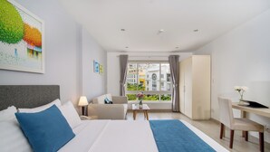 Quarto de hotel com cama, escrivaninha, cadeira, mesa pequena e vista para edifícios pela janela.