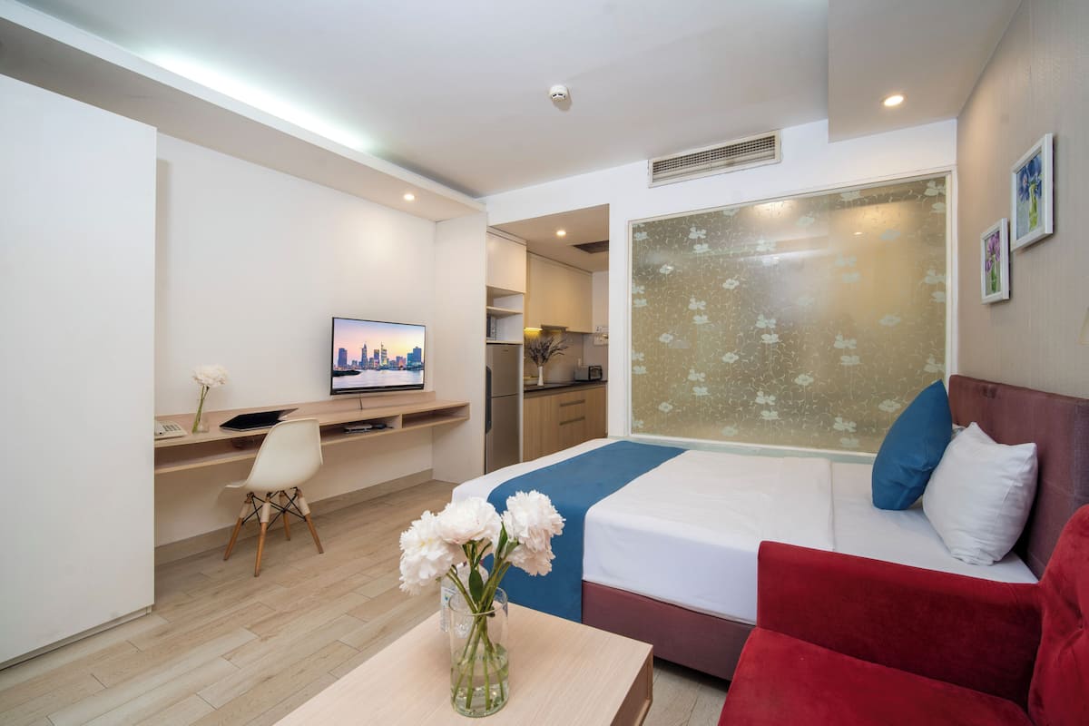 Habitación de hotel con cama, escritorio, silla, televisor y ventana con vistas a la ciudad.