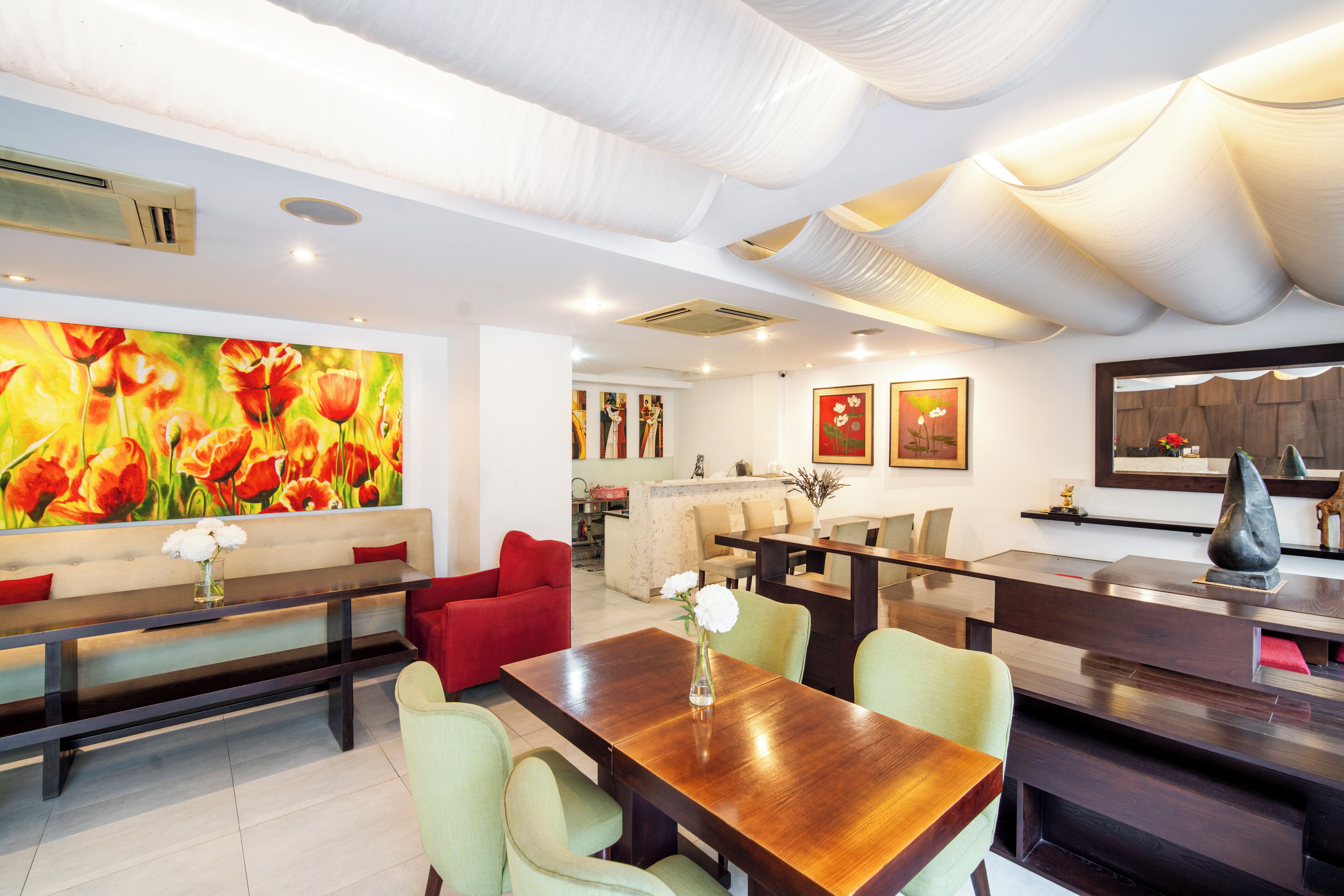 A modern living room with a wooden dining table, red and green chairs, a bench, and a large floral painting on the wall.