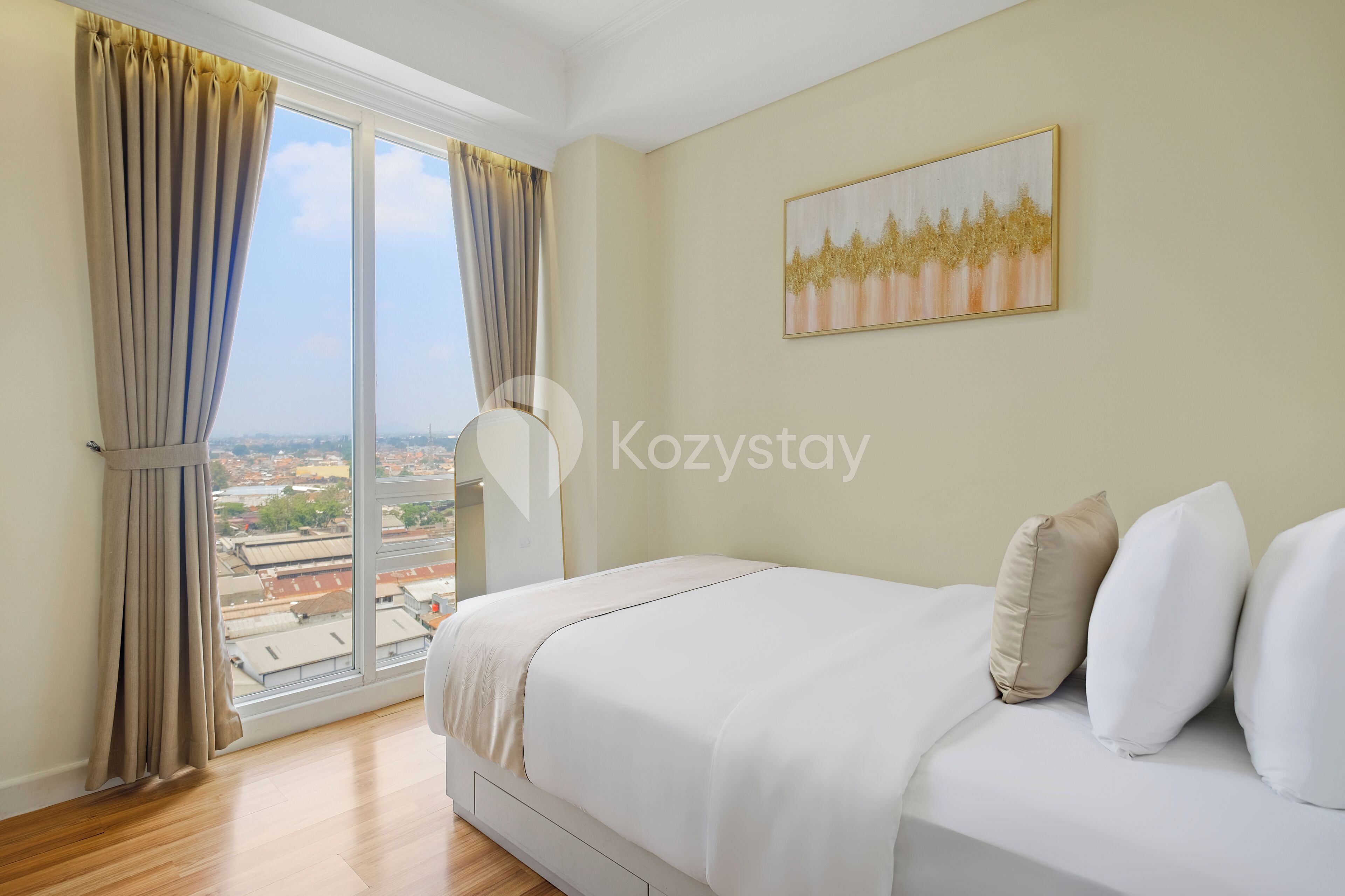 A bedroom with a large window, a bed with white bedding, and a painting on the wall.