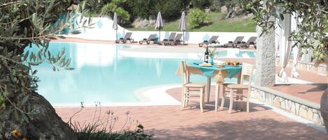 Un espace aménagé au bord de la piscine, avec des chaises longues et des parasols, une table avec des chaises, et une vue sur la piscine.