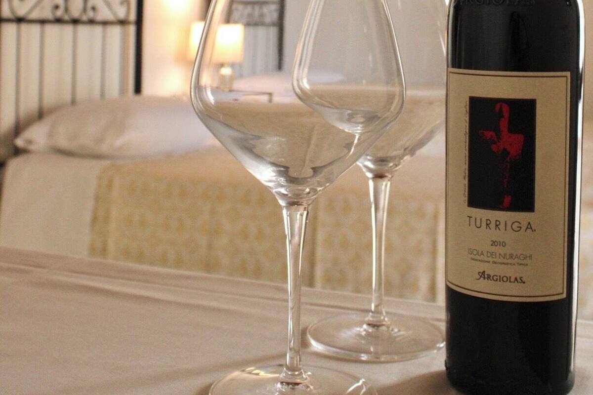 Una botella de vino y dos copas sobre una mesa en una habitación con cama y un cuadro en la pared.