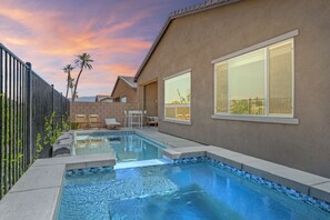 Une maison moderne dotée d’une piscine, de grandes fenêtres et d’un patio aménagé avec du mobilier d’extérieur.