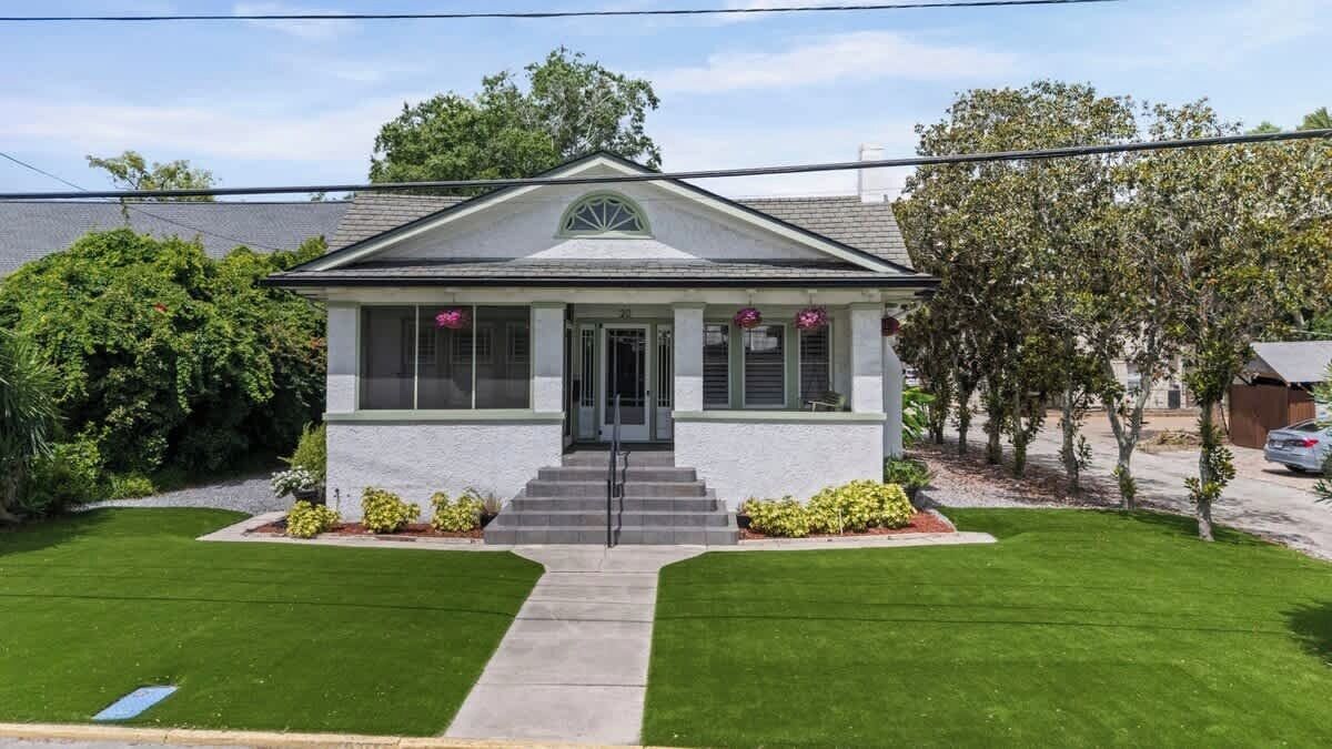 A two-story house with a front porch, a central entrance, and a small front yard with a lawn and shrubs.