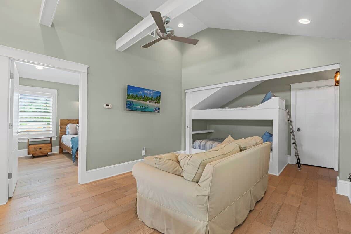 A room with a bunk bed, a sofa, a ceiling fan, and a painting on the wall.