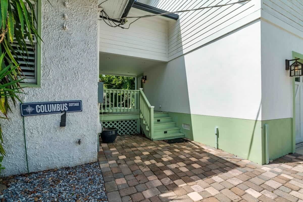 A white building with a green porch, a sign reading 'Columbus Cottage,' and a brick pathway leading to the entrance.
