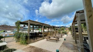 An outdoor patio area with wooden tables and benches, a covered seating area, and a view of the surrounding buildings and landscape. - The Zorn cocoon (Monswiller)