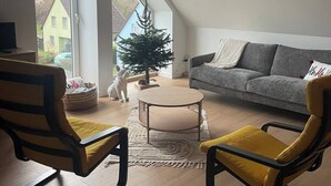 A modern loft apartment with a sloped ceiling, a large window, a small Christmas tree, a grey sofa, and two yellow armchairs. - The Zorn cocoon (Monswiller)