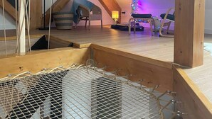 A loft bedroom with a sloped ceiling, wooden beams, a hammock, a small table, and a chair. - The Zorn cocoon (Monswiller)