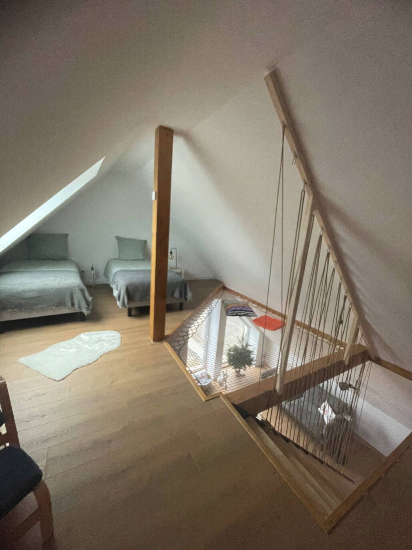 A small attic bedroom with a sloped ceiling, a wooden ladder, and a small window.