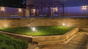 A well-lit outdoor area with a stone wall, a grassy area, and lounge chairs under a pergola.