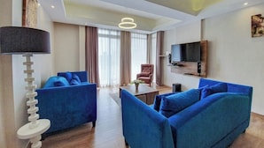 A modern living room with blue sofas, a coffee table, a lamp, and a TV mounted on the wall.