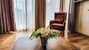 A room with a wooden floor, a brown armchair, and a vase with white flowers and green foliage.