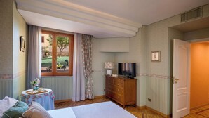 Ein Schlafzimmer mit Bett, Kommode, Fernseher und einem Fenster mit Vorhängen.