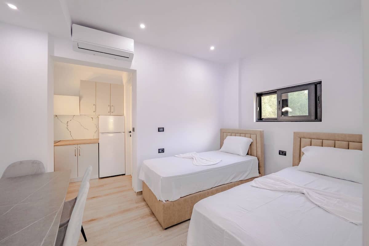 Een moderne, minimalistisch ingerichte slaapkamer met twee bedden, een kleine kitchenette en een eethoek.