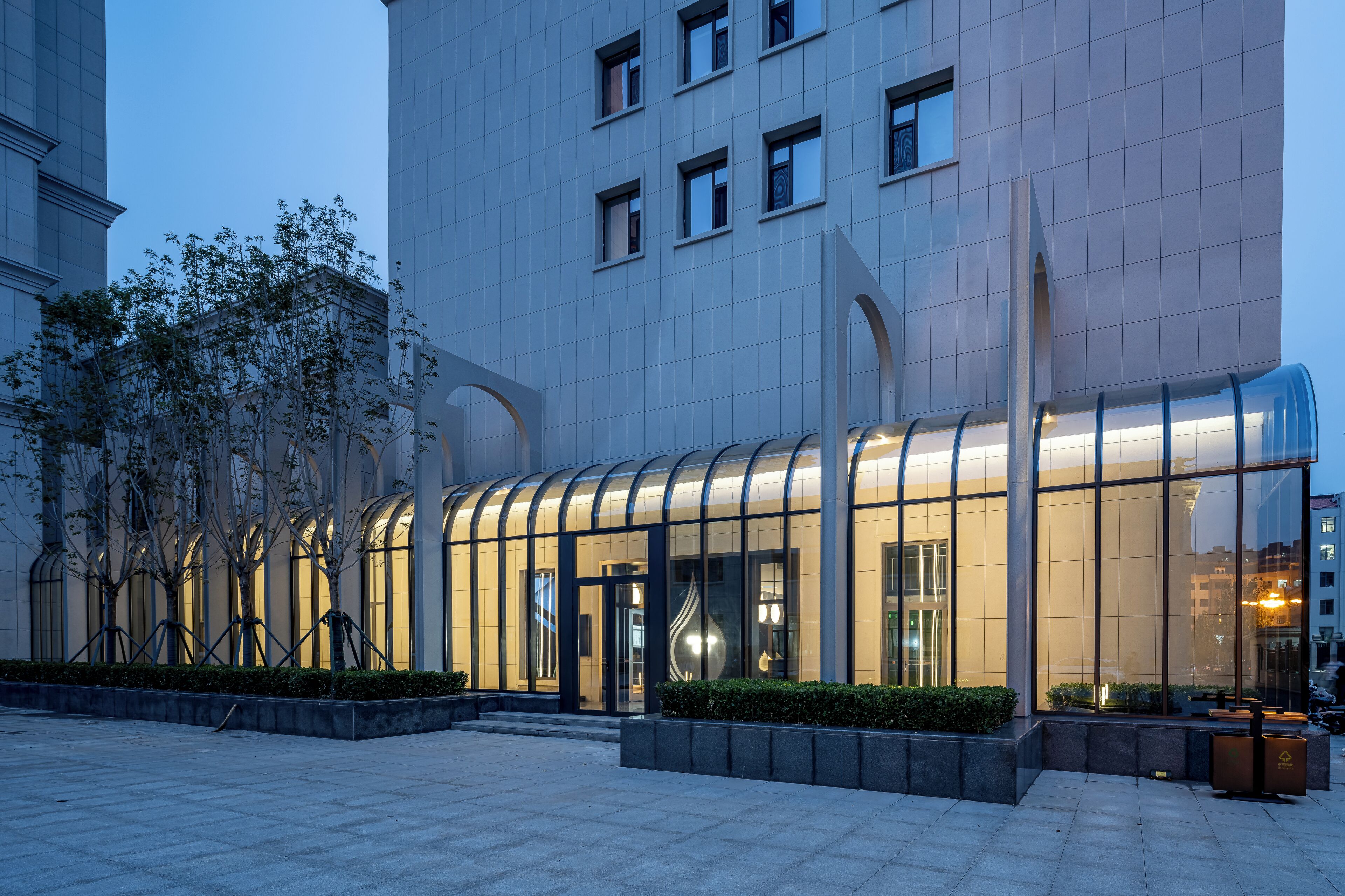 A modern building with a curved glass facade, a well-maintained courtyard with trees, and a clean, tiled ground.