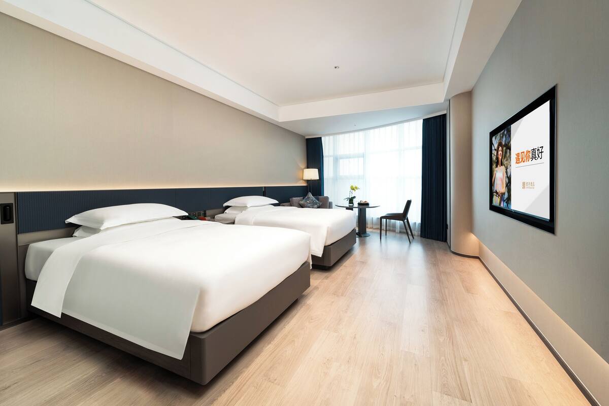 A hotel room with two beds, a desk, and a TV on the wall.