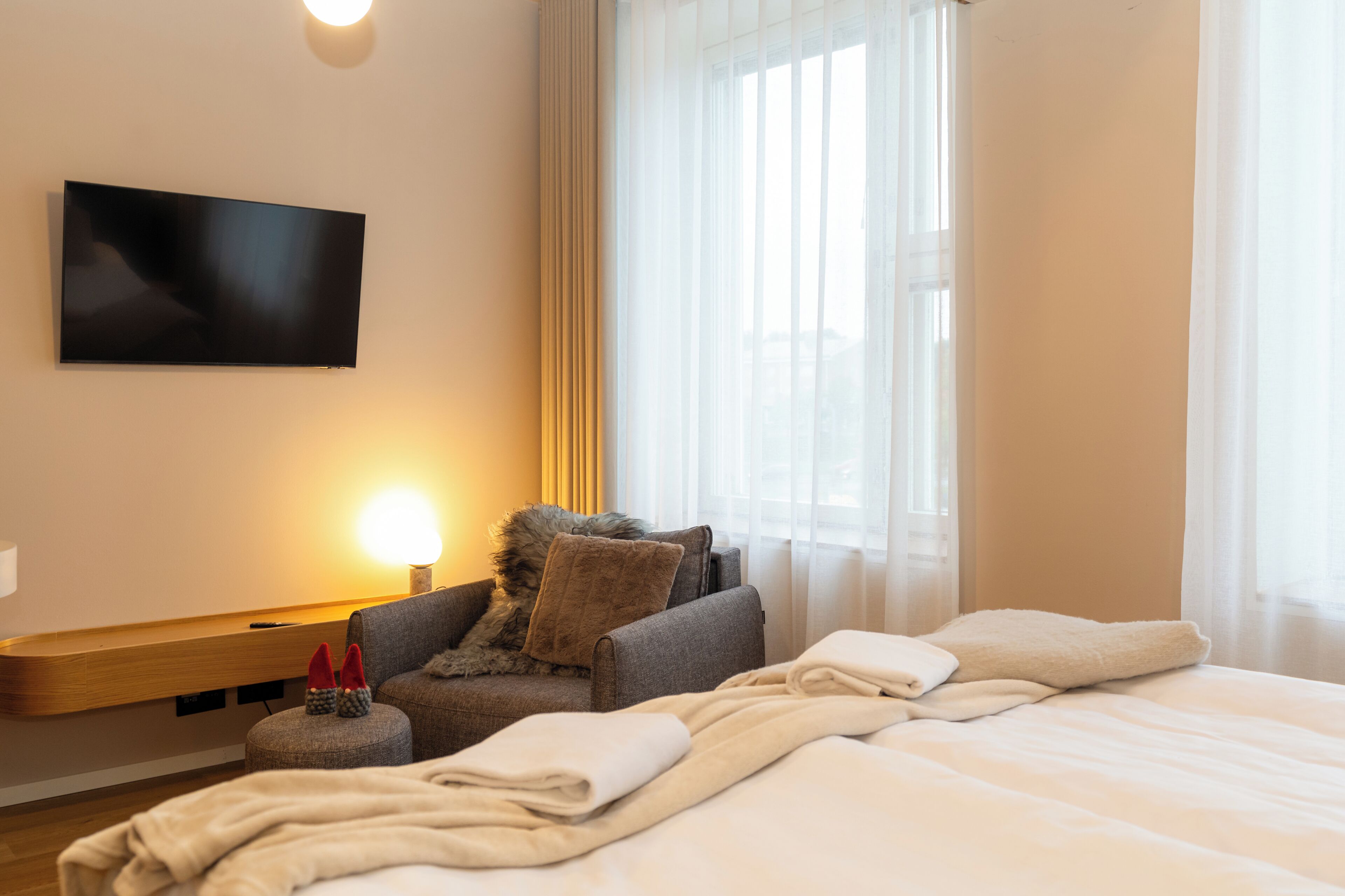 A hotel room with a bed, a sofa, a TV mounted on the wall, and a window with curtains.