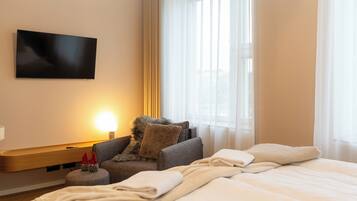 A hotel room with a bed, a sofa, a TV mounted on the wall, and a window with curtains.