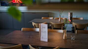 Een restaurantinterieur met houten tafels, stoelen, een menukaartstandaard, een vaas met bloemen en een glas.