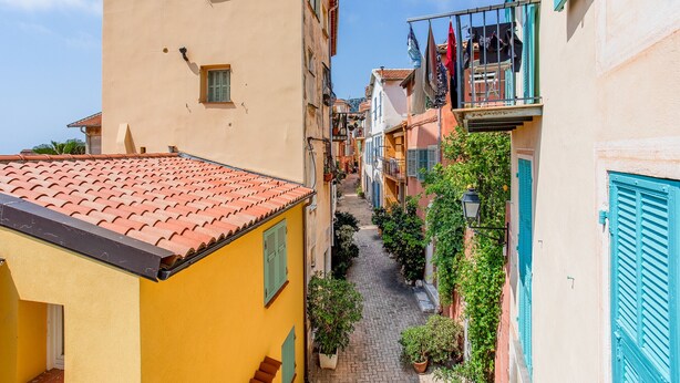 A narrow cobblestone street flanked by colorful buildings with shutters and balconies.