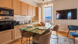 A modern kitchen with wooden cabinets, a glass dining table, and a flat-screen TV mounted on the wall.