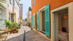 A narrow cobblestone street with a bed in a room with green shutters.