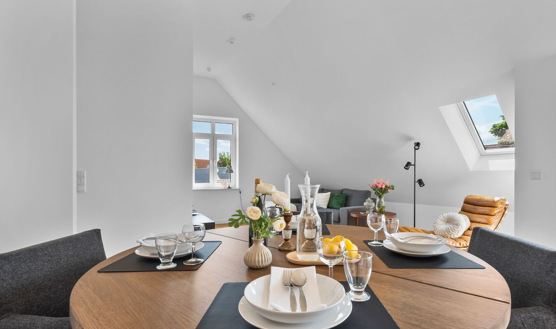 A modern dining area with a round table set for four, a sofa, and a chair in the background.