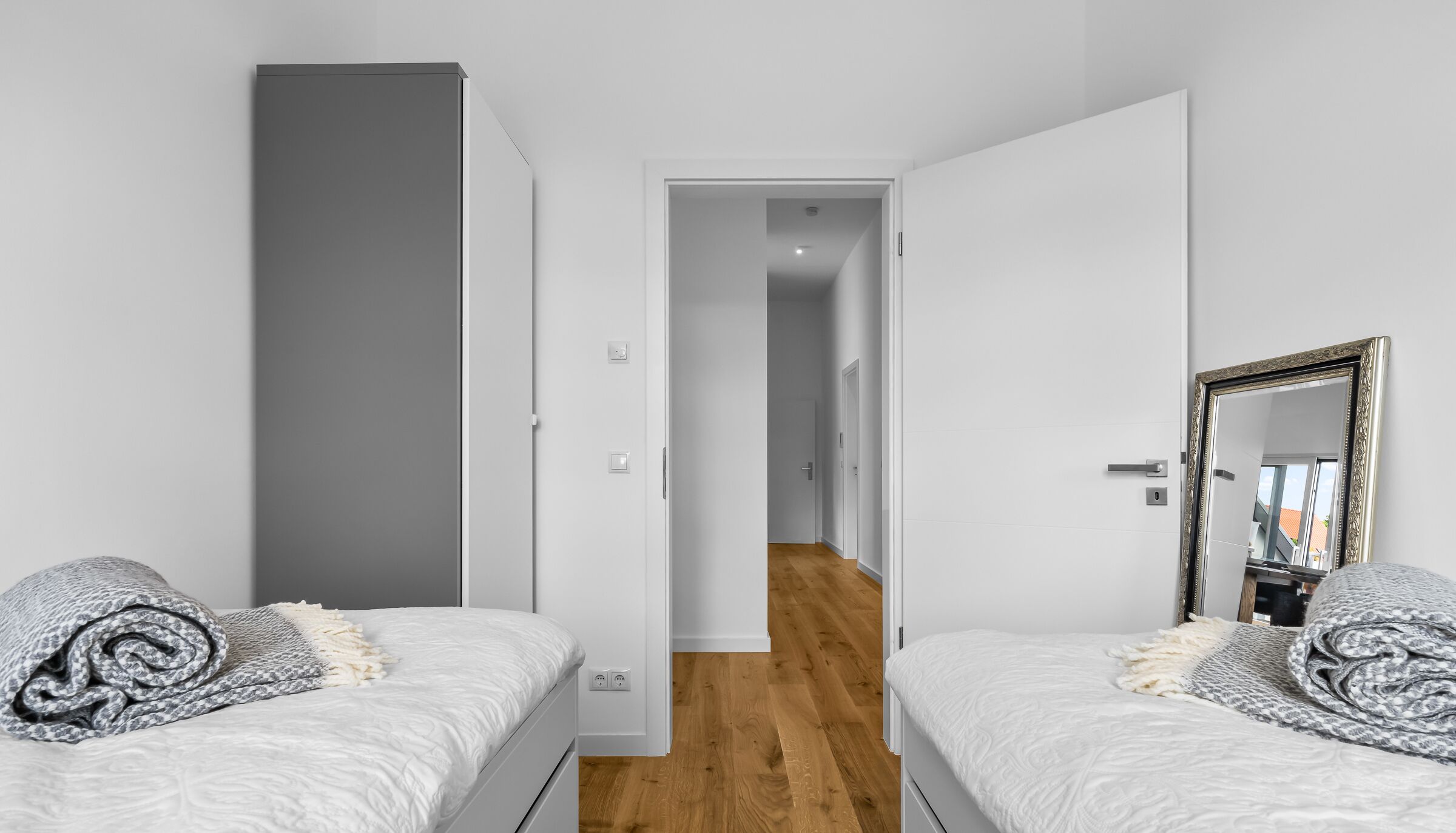 Ein modernes Schlafzimmer mit zwei Betten, Holzboden und einem Flur, der in ein weiteres Zimmer führt.