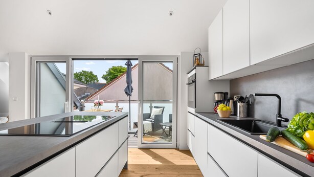 A modern kitchen with white cabinets, a black countertop, and a sliding glass door leading to an outdoor seating area. - "Strandhafer" in Heiligenhafen - high-quality and ultra-modern temporary apartment (Heiligenhafen)
