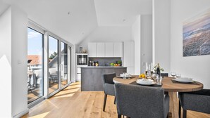 A modern kitchen with a central island, a dining area with a round table and grey chairs, and a large sliding glass door leading to an outdoor space. - "Strandhafer" in Heiligenhafen - high-quality and ultra-modern temporary apartment (Heiligenhafen)