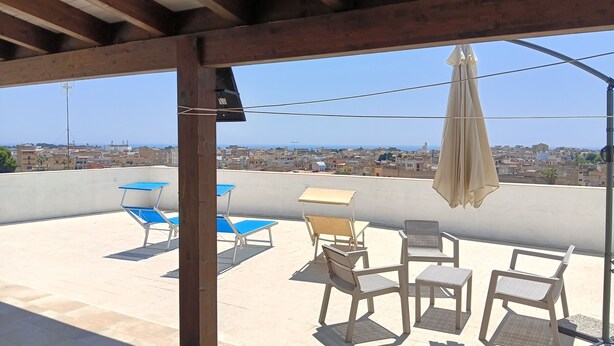 Une terrasse sur le toit offrant une vue sur le paysage urbain, aménagée avec du mobilier d’extérieur et une structure en forme de pergola.