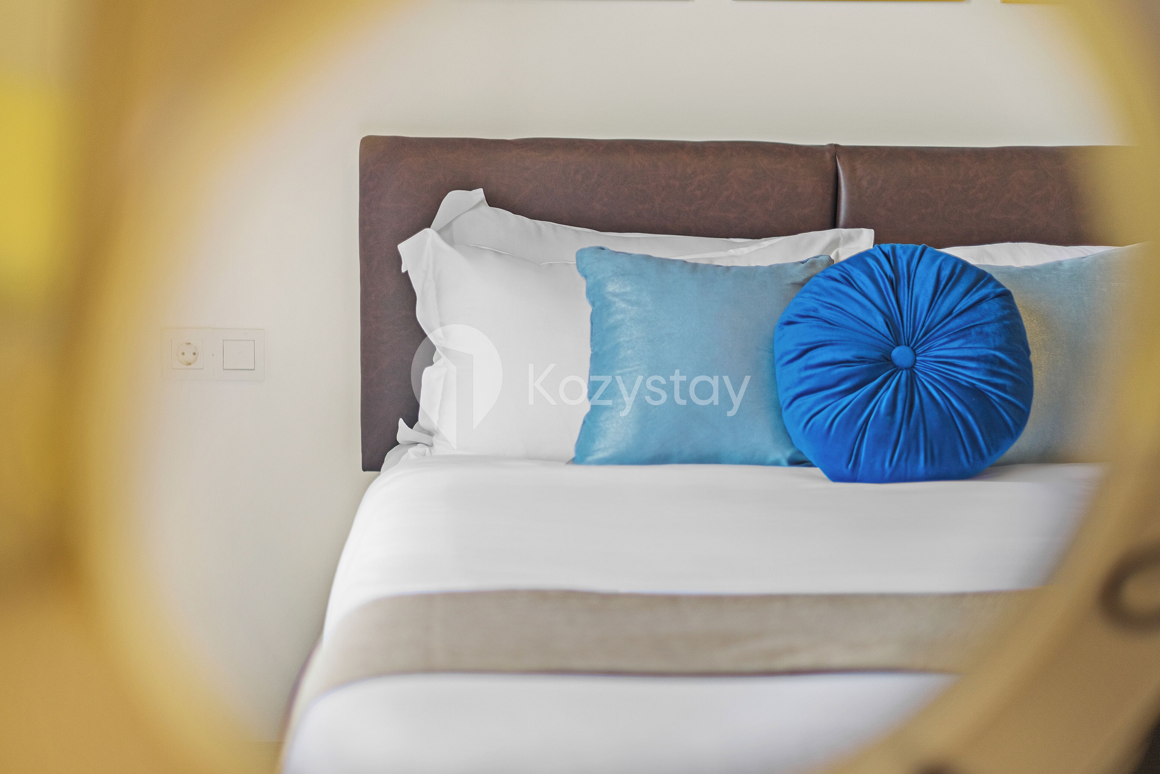 Un lit avec une tête de lit marron, des oreillers blancs et bleus, et un coussin décoratif bleu.