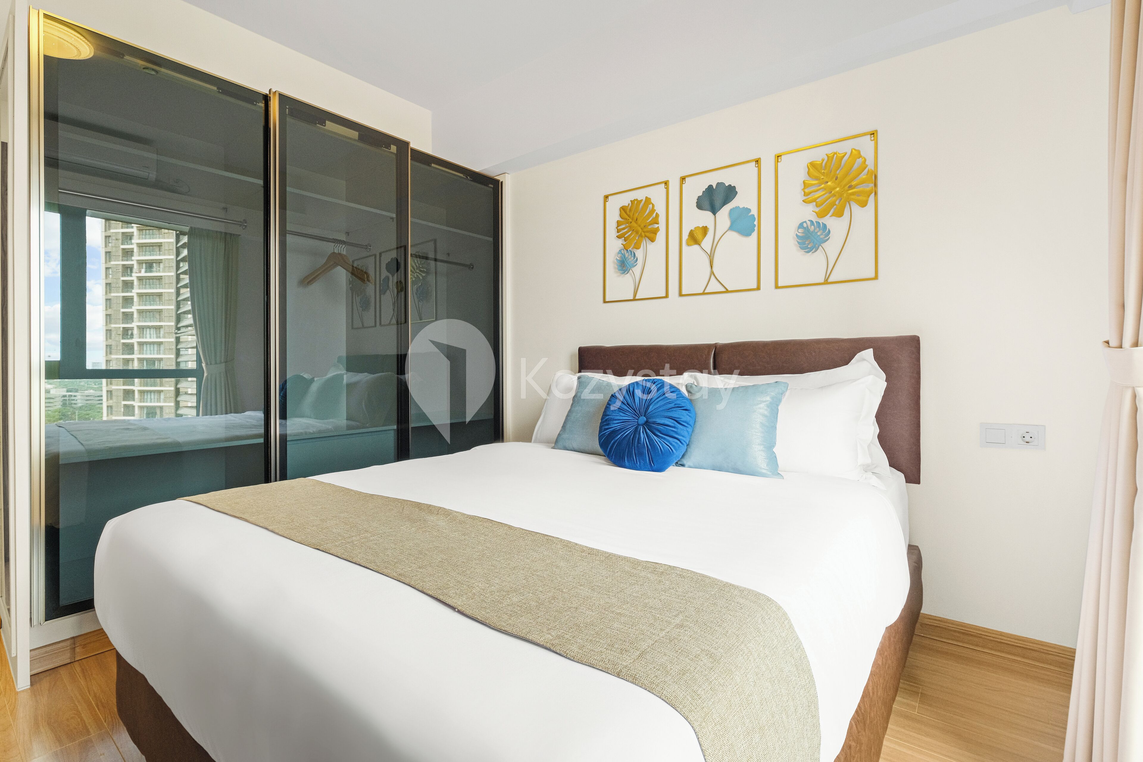 Ein Hotelzimmer mit einem großen Bett, einer Schiebetür zu einem Balkon und drei gerahmten Blumenbildern an der Wand.