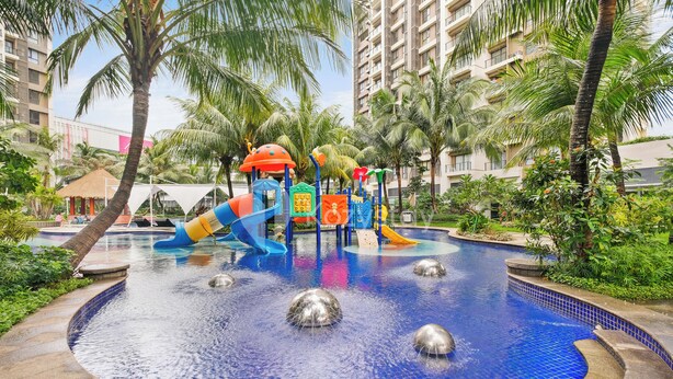 Un espace de jeux pour enfants avec des toboggans et des structures d’escalade, entouré de palmiers et d’une piscine.