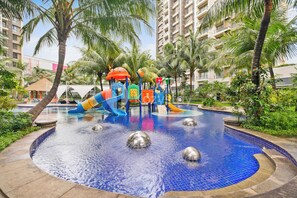 A children's play area with slides and climbing structures, surrounded by palm trees and a pool. - Solace by Kozystay - BSD (Pagedangan)