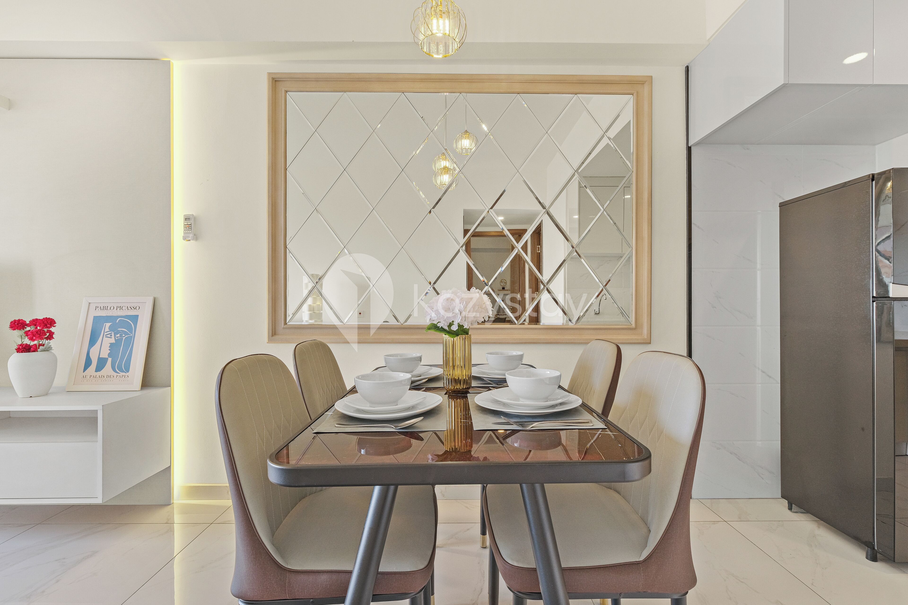 Comedor con una mesa dispuesta para cuatro personas, una lámpara moderna y un espejo grande con diseño geométrico.