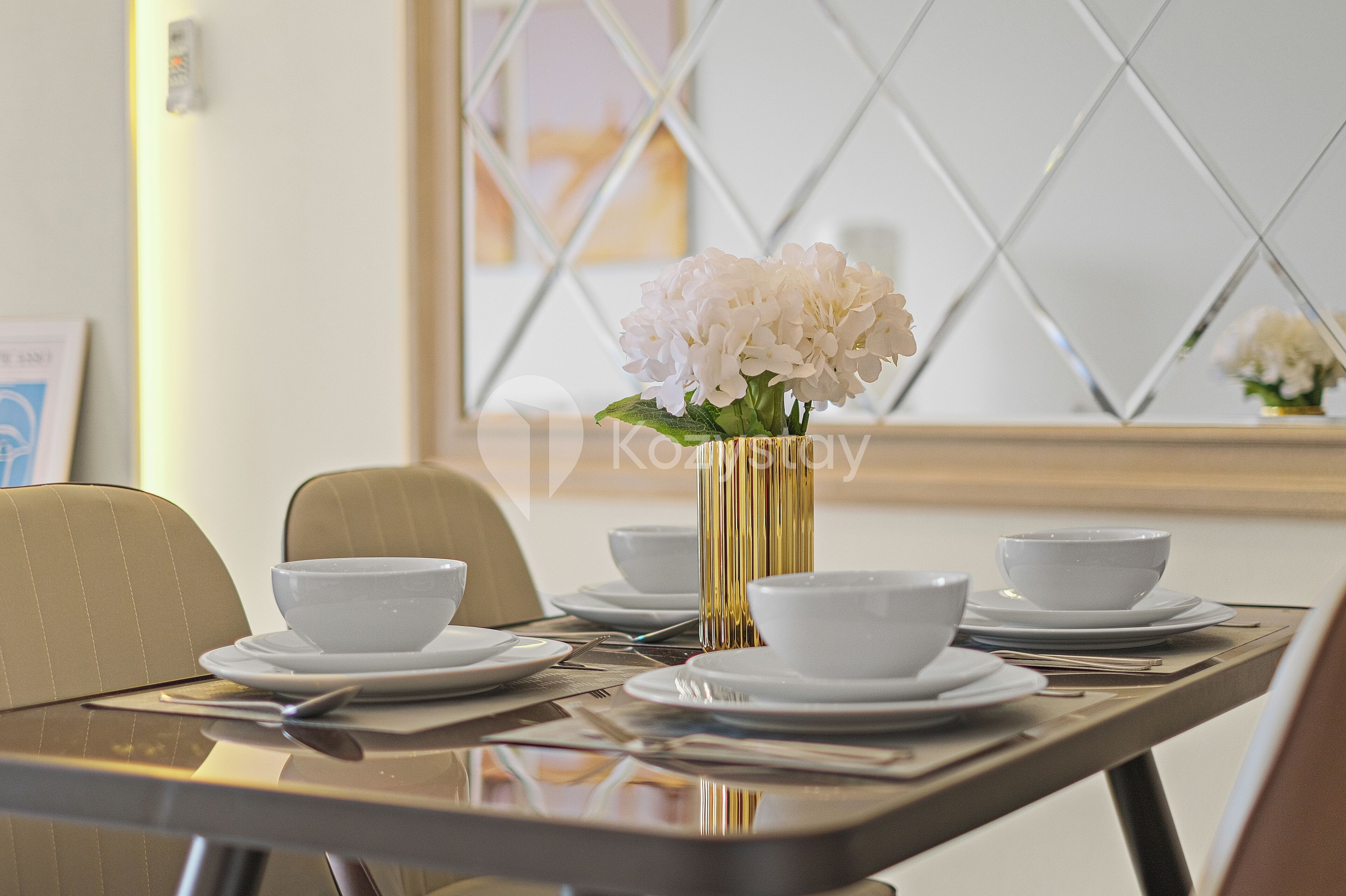 A dining table set with white plates, bowls, and cutlery, with a vase of white flowers in the center.